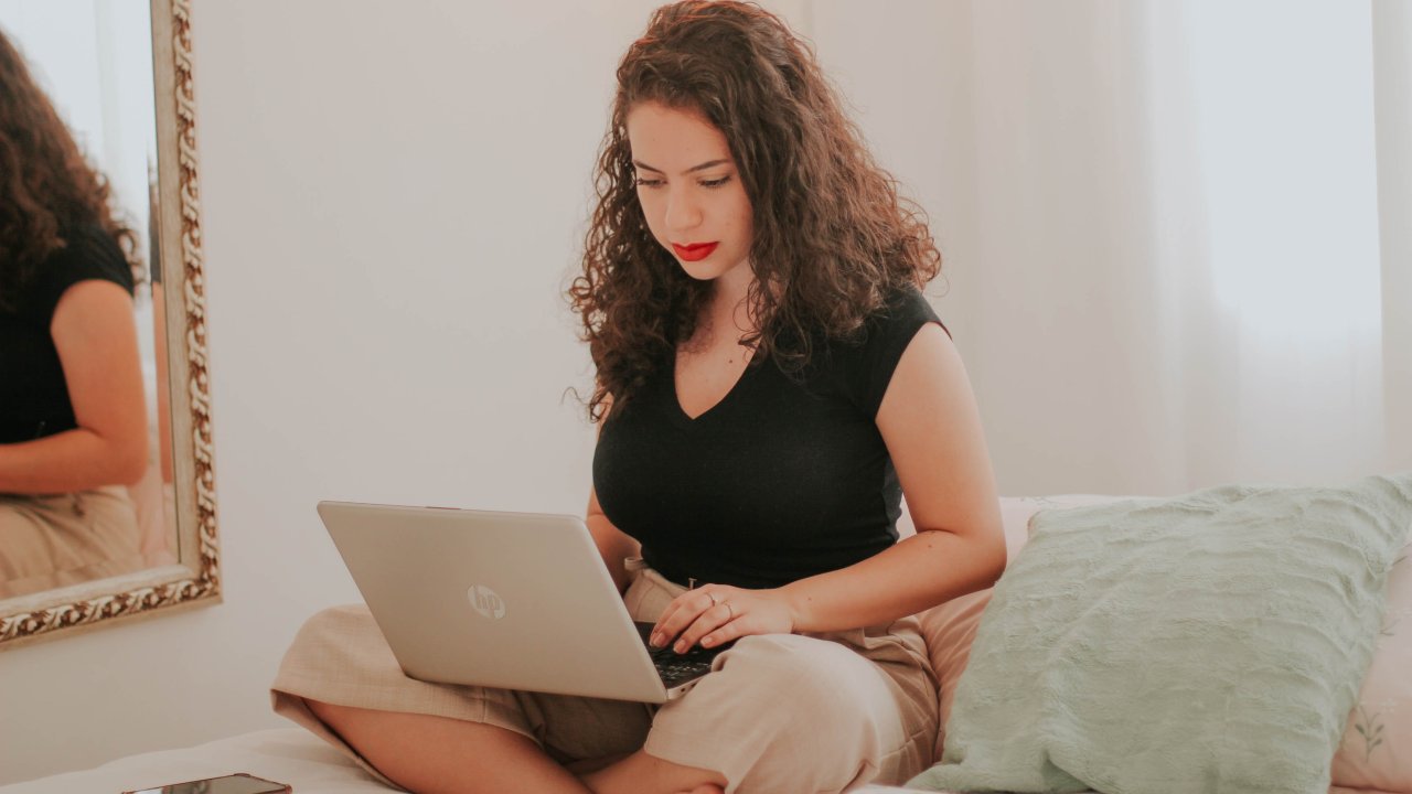 Foto de mulher sentada de pernas cruzadas em sofá, com laptop no colo