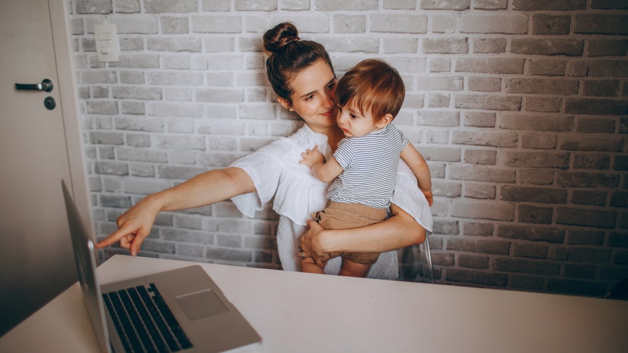 foto de mãe com o filho no colo apontando o dedo para um notebook